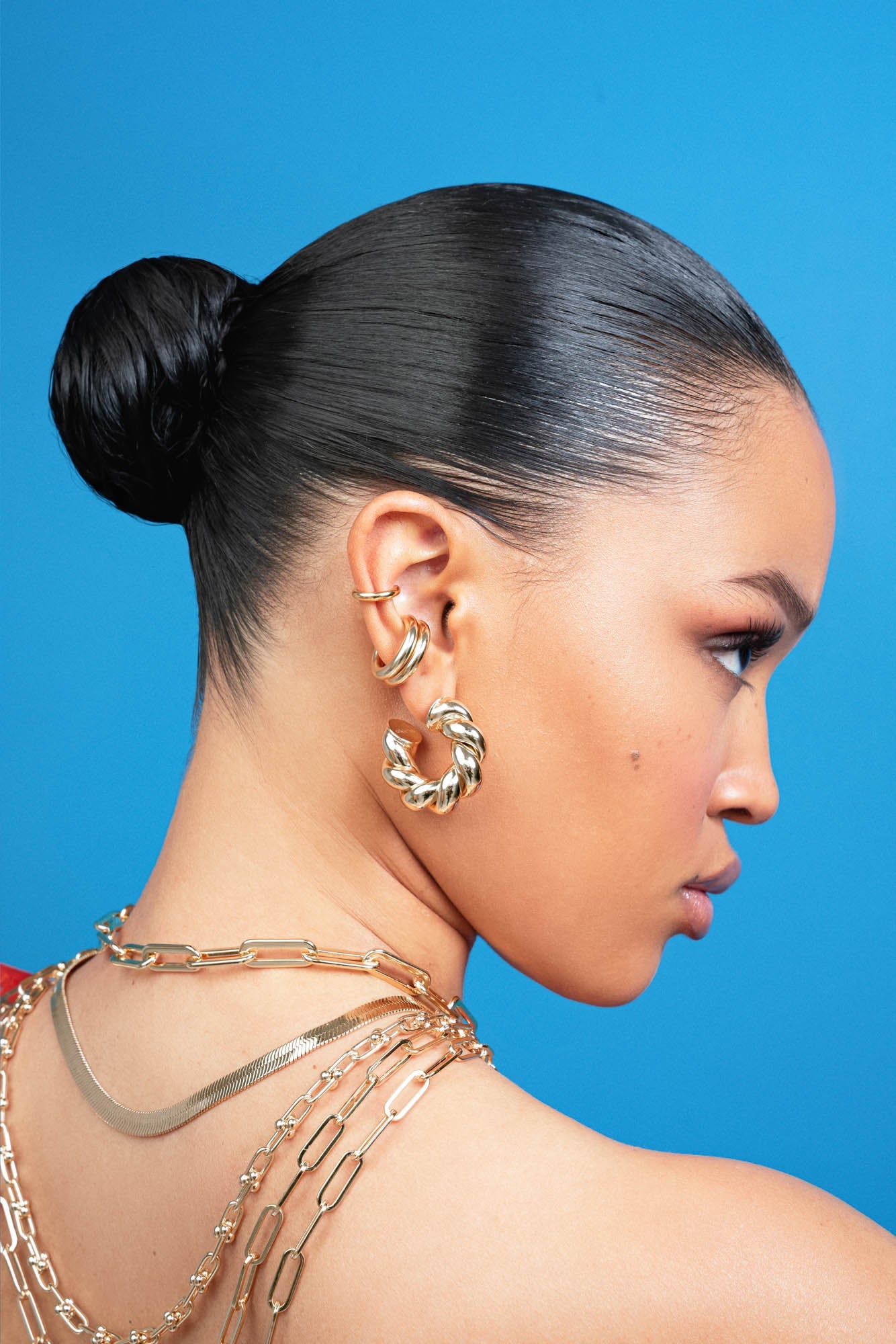 Model wearing Tallulah Hoops by Eklexic in gold with layered chain necklaces. Bold hoop earrings handcrafted from sustainable brass.