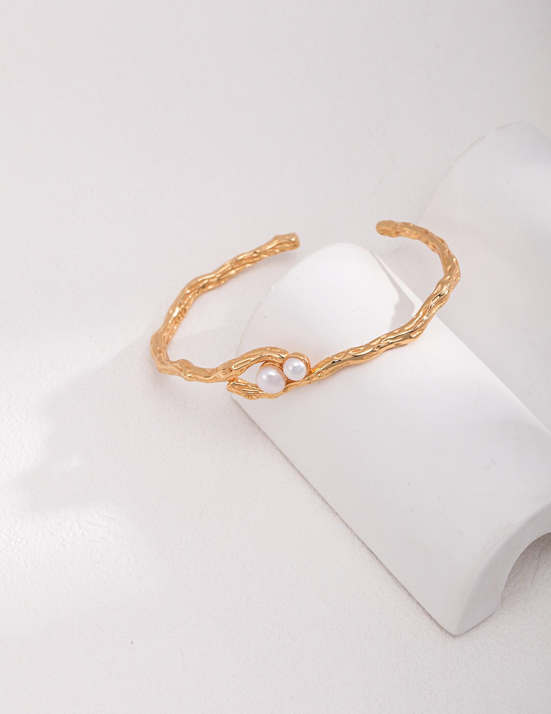 Handmade Double-Pearl Cuff Bracelet with natural freshwater pearls and textured 18k gold-plated band, shown on curved white display.
