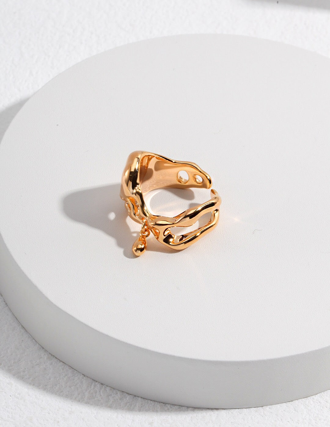 Teardrop Ring - Minimalist Pendant in 18k gold-plated finish with irregular open band and dangling charm, displayed on white round platform.
