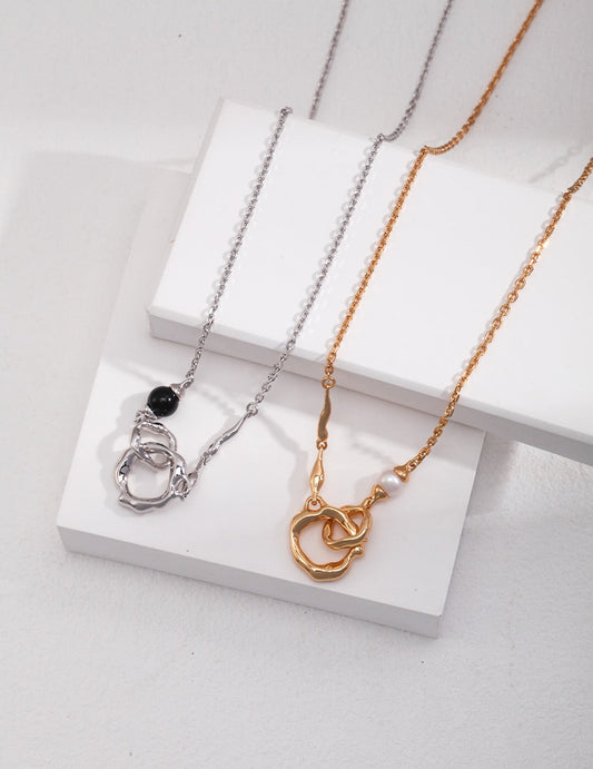 Roundness Hollow Round Black Onyx / Pearl Necklace in gold and silver with asymmetrical design and gemstone accents, displayed on white blocks.