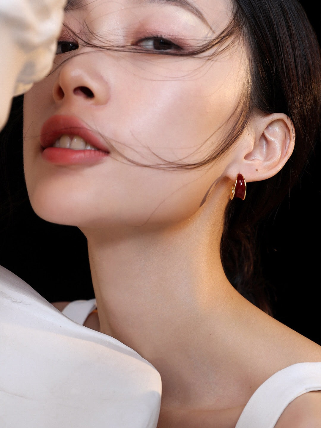 Model wearing Helix Red Drip Glaze Earrings, showcasing the bold spiral hoop design with gold detailing and a luxurious handmade finish.
