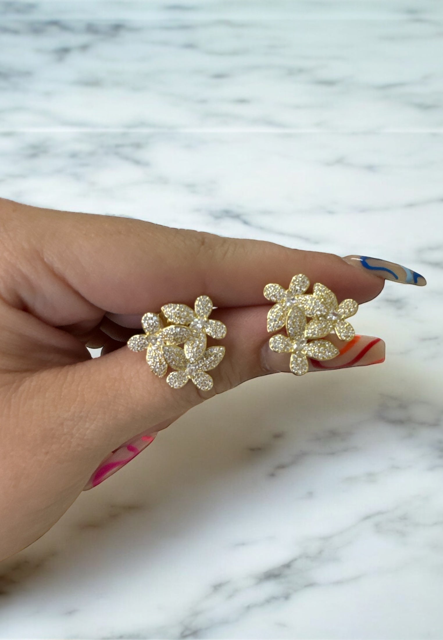 Hand holding gold flower stud earrings with shimmering cubic zirconia petals, showcasing size and sparkle.