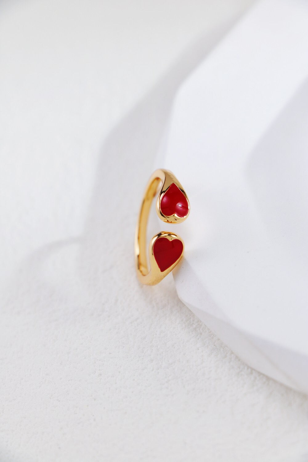 Adjustable Gold Vermeil Heart Ring featuring two red heart-shaped ends, ideal for US sizes 5.5-8, shown upright on a textured white background.