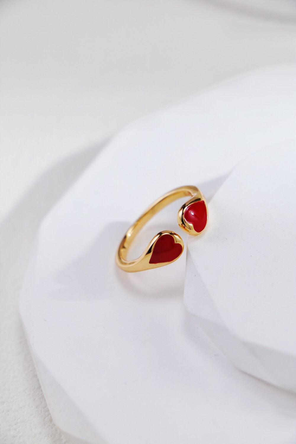 Close-up of the Gold Vermeil Adjustable Heart Ring with vibrant red enamel hearts, handmade and tarnish-resistant, resting on a white platform.