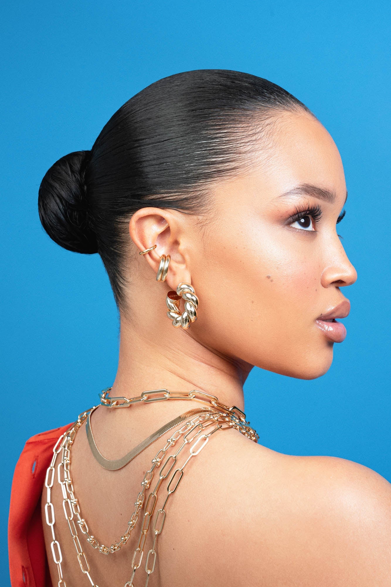 Side profile of model showcasing Tallulah Hoops by Eklexic in gold, styled with layered gold chains. Statement hoop earrings in sustainable brass.