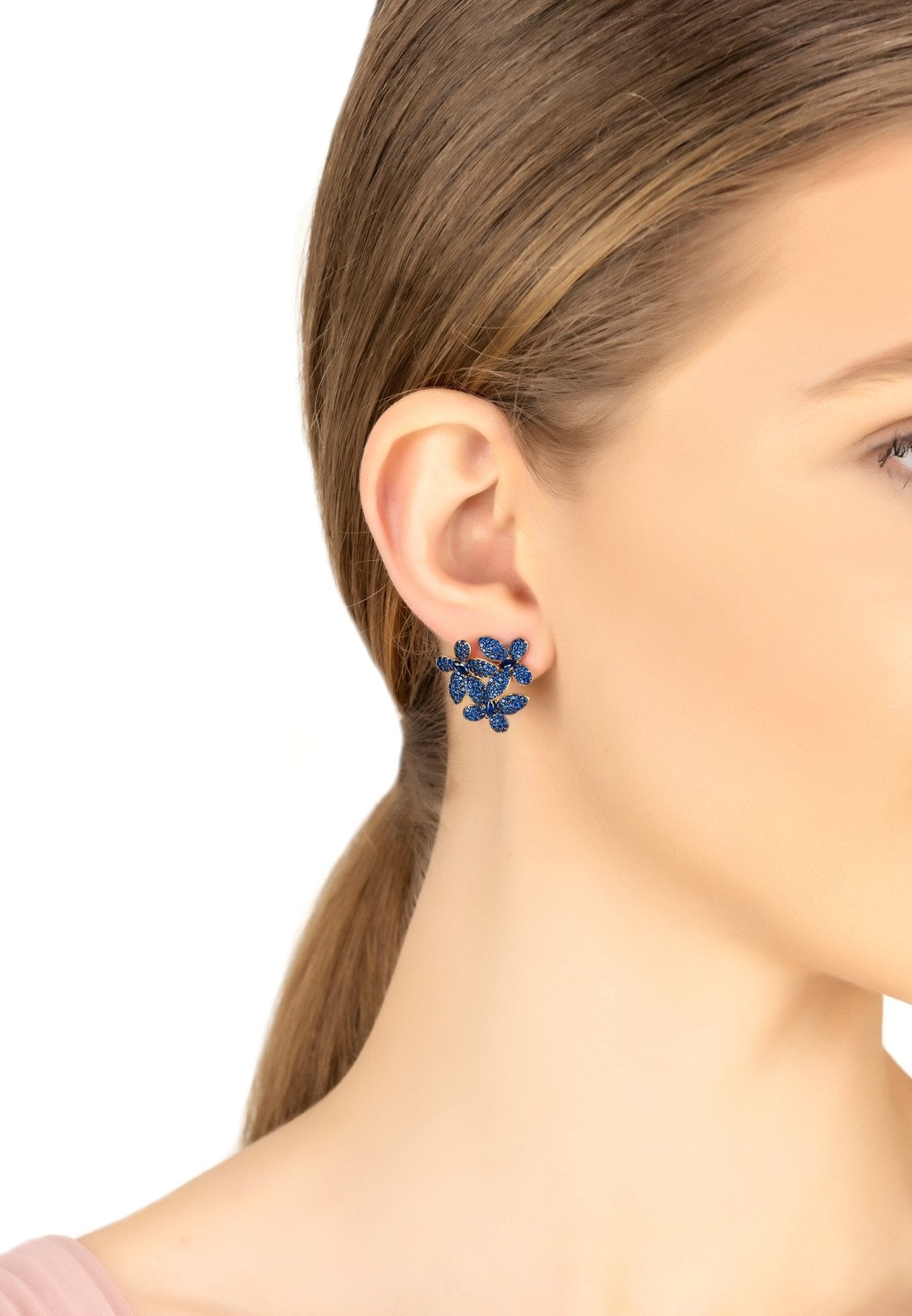 Model wearing sapphire blue flower stud earrings with gold accents, showcasing elegant and timeless bridal or evening jewelry.